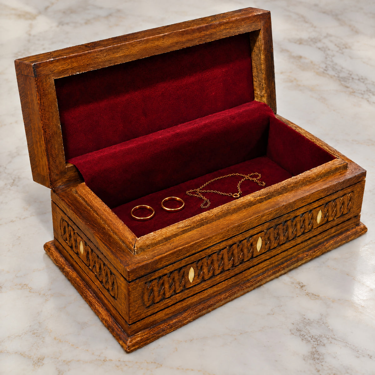 Opulent Carved Box open on marble, wine-red velvet lining with two rings and a chain