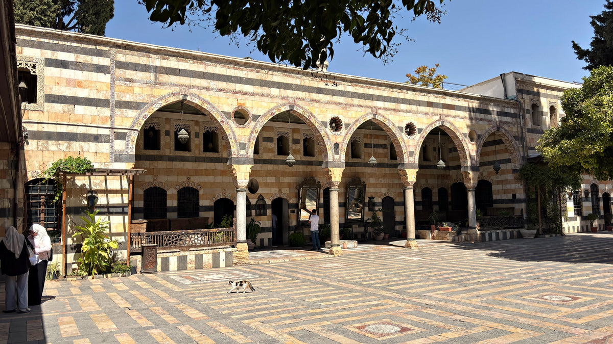 An arcade of pointed arches around the striped stone courtyard of Azm Palace