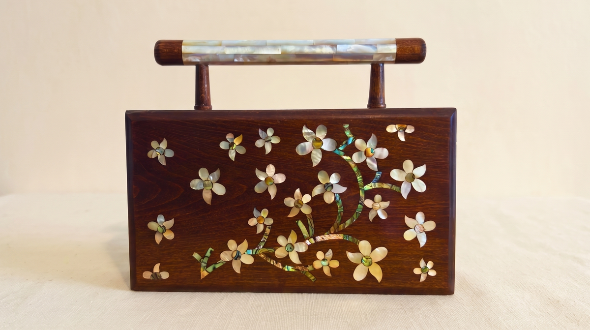 Walnut clutch with mother-of-pearl flowers and a mother-of-pearl handle, on cream linen