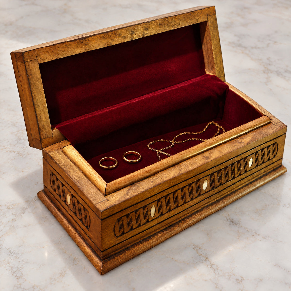 Regal Carved Box open on marble, wine-red velvet lining with two rings and a chain