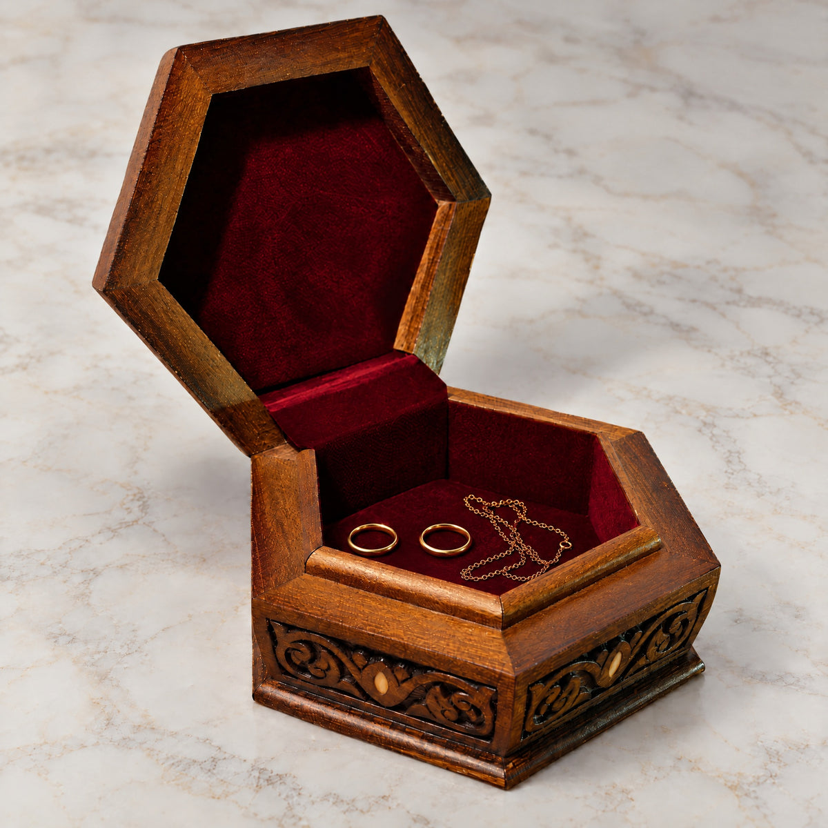 Orchard Carved Box open on marble, wine-red velvet lining with two rings and a chain