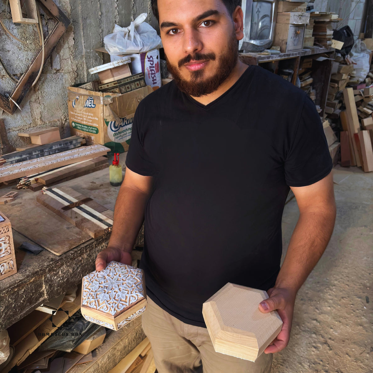 Mohammad Tarek Al-Dahh holding two carved boxes in his workshop in Damascus