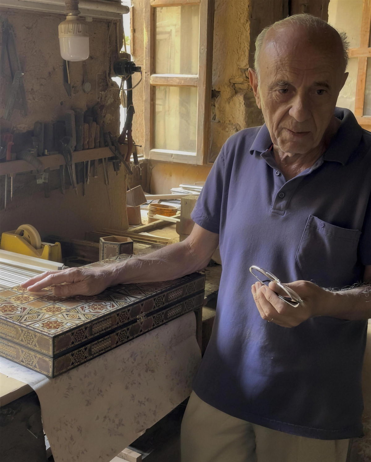 Gabriel Al-Dayeh (Abu Boutros) at his workbench in Damascus, one hand on a mosaic backgammon board