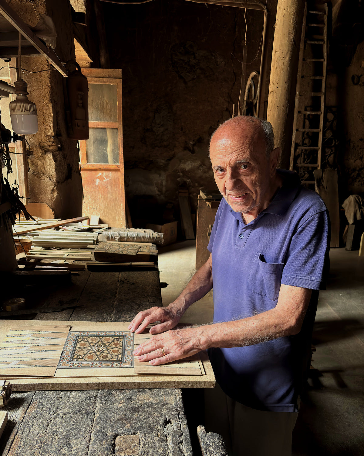 Gabriel Al-Dayeh (Abu Boutros) at his workbench in Damascus, hands on a mosaic backgammon board